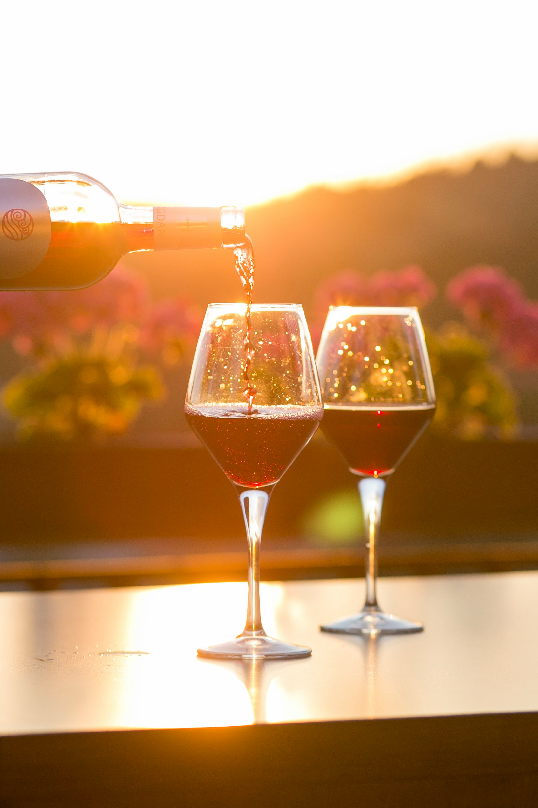 Red wine being poured into glasses with the setting sun in the background. Title: Pouring Red Wine at Sunset