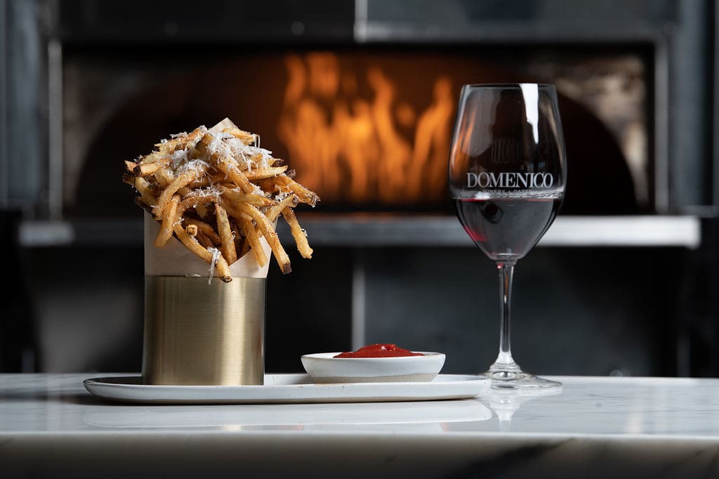 Glass of Domenico dry wine and truffle fries shot in front of pizza at Osteria Domenico Restaurant