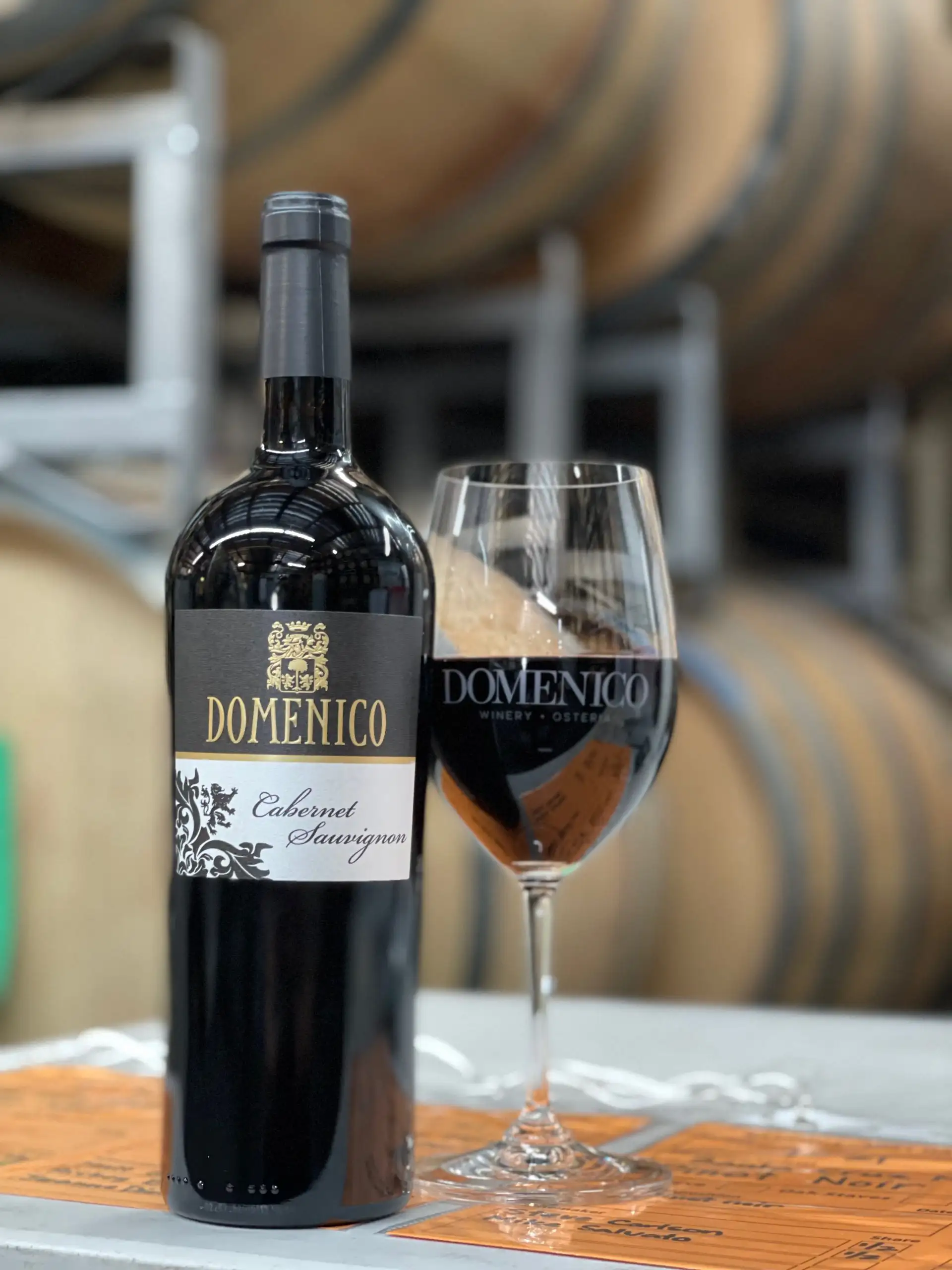 Bottle of Domenico Cabernet Sauvignon red wine next to a filled wine glass in a winery cellar