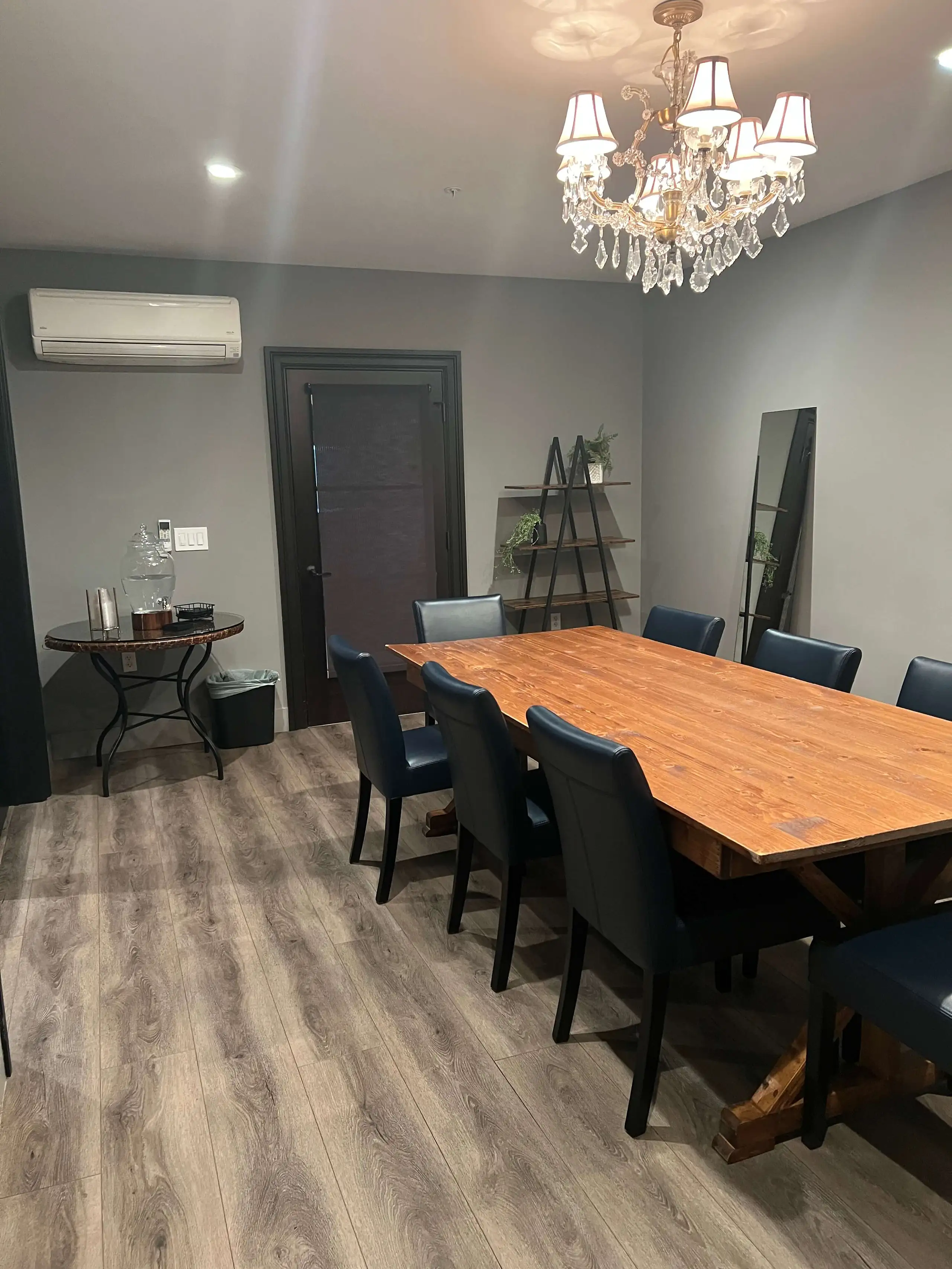 Private dining room with a long wooden table, black chairs, chandelier lighting, and modern decor.