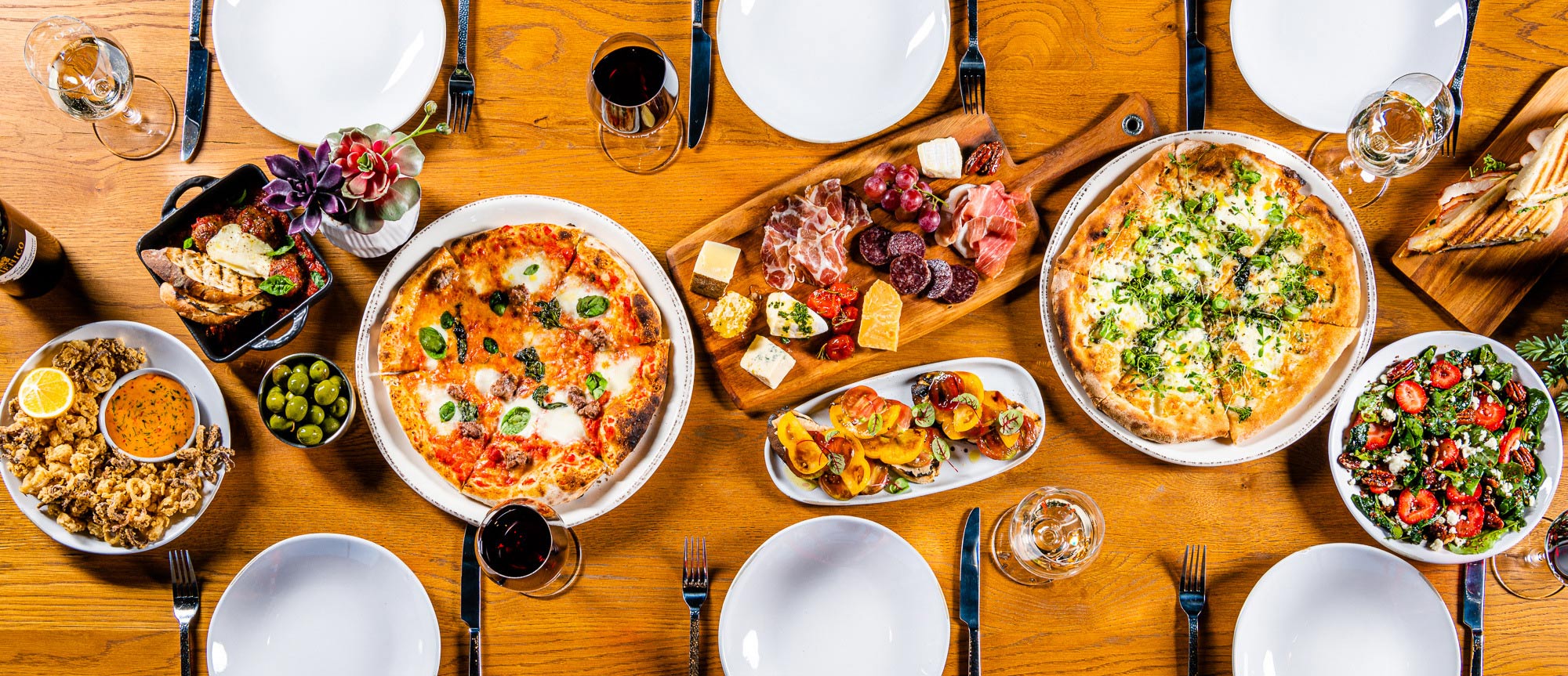 Plated dining table with pizza, charcuterie, wine, calamari, and salad.