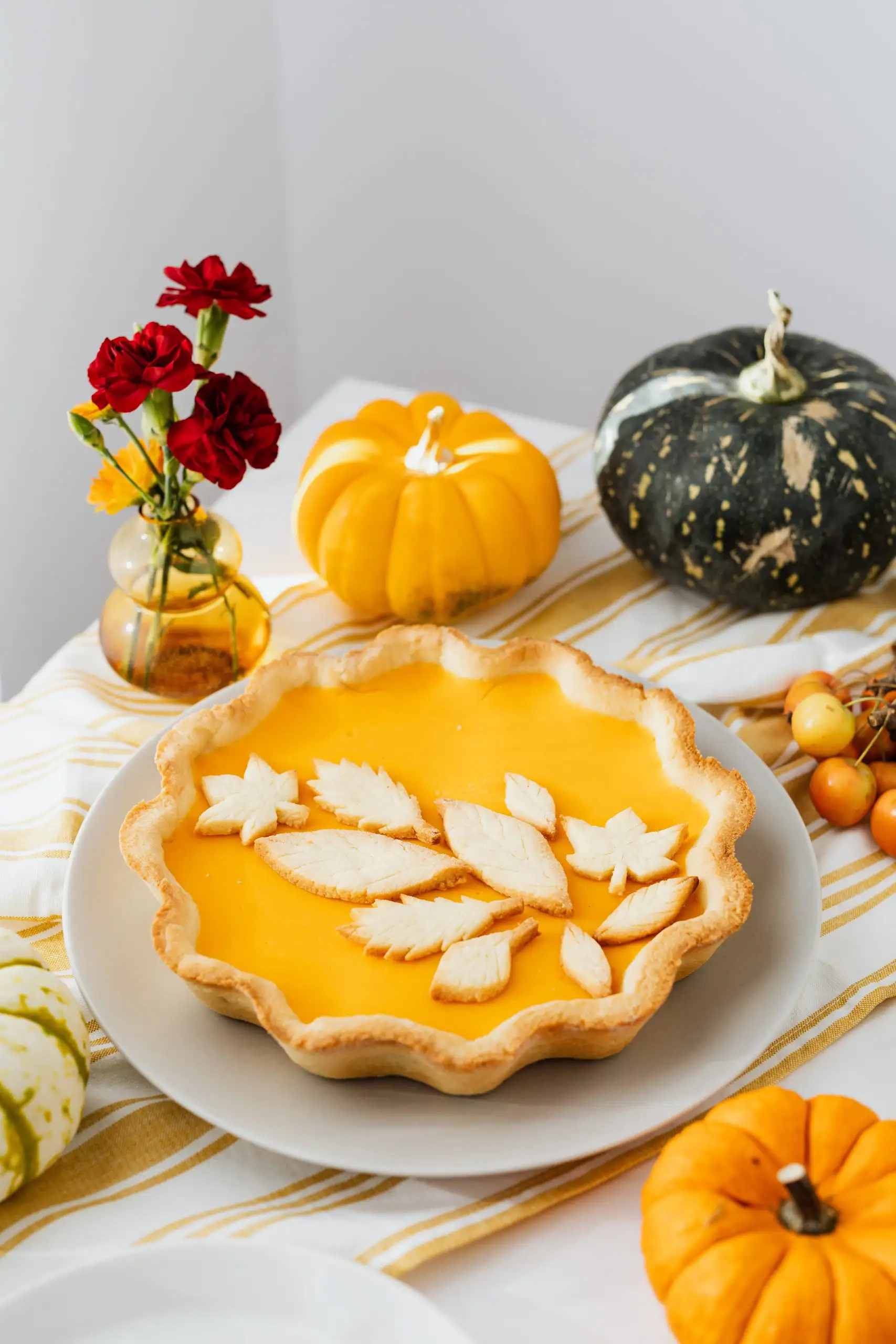 A beautifully arranged pumpkin pie with a decorative leaf-shaped crust, set against autumn-themed decor.