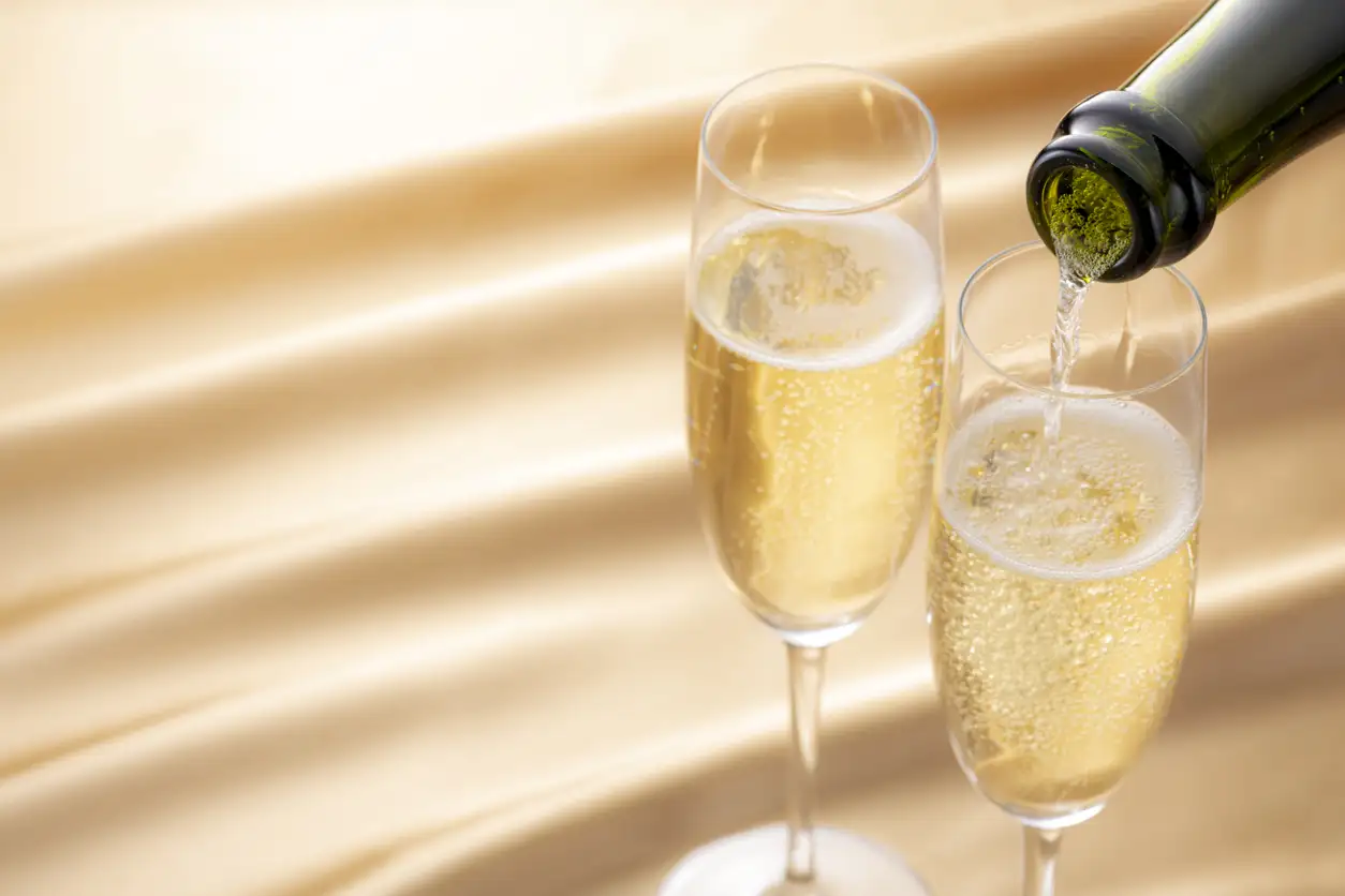 Champagne being poured into two flutes with bubbles rising in a bright, elegant setting.