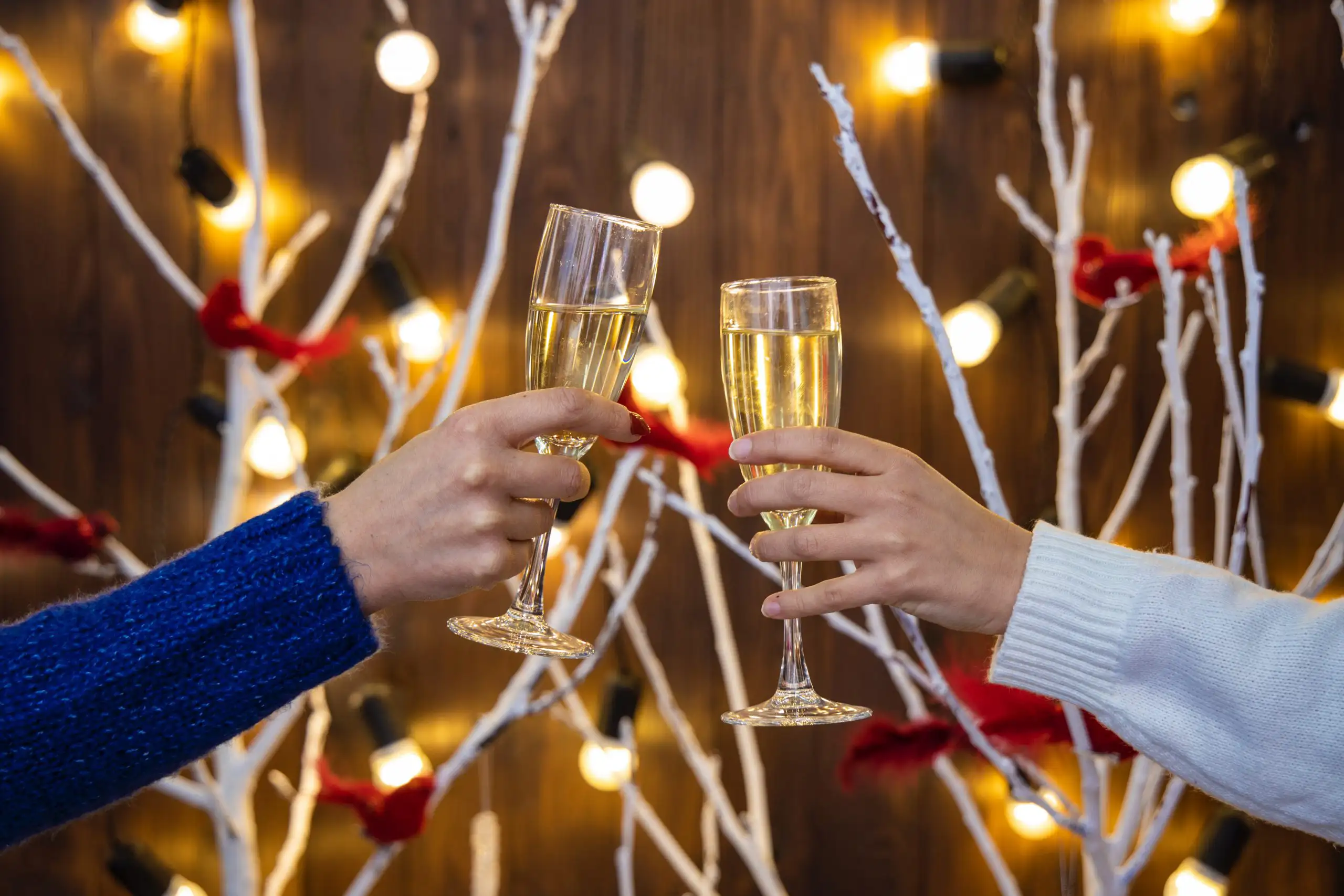 Two people toasting champagne glasses in front of festive lights