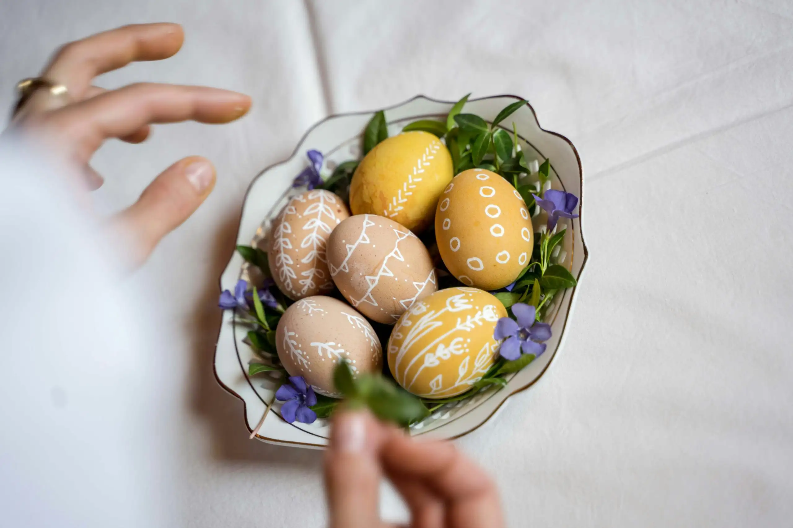 Spring Easter table setting with floral plates, wrapped candy, wine glass, and pastel napkin on a white tablecloth.