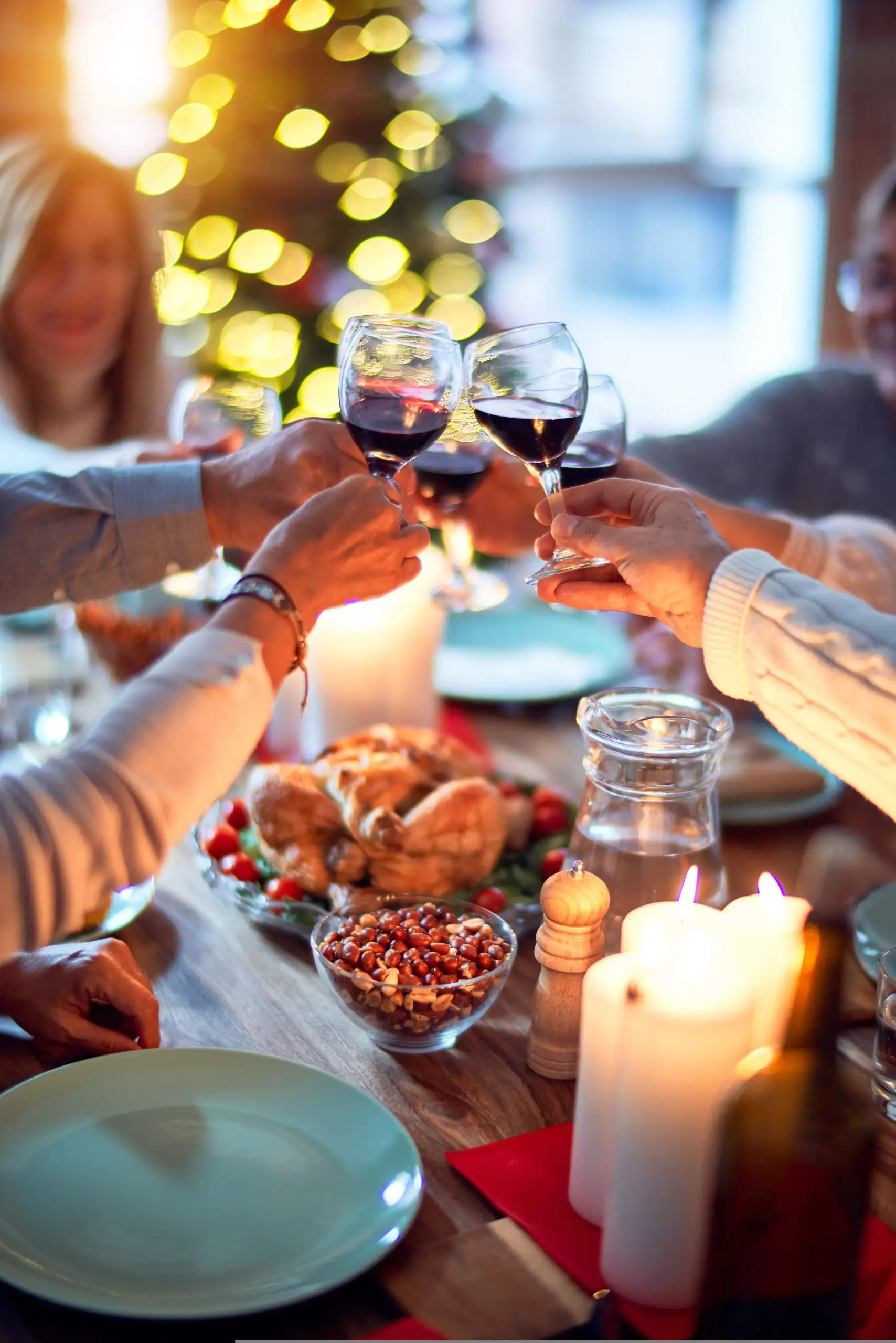 Family members toasting with red wine glasses over holiday dinner table with roasted chicken and candles