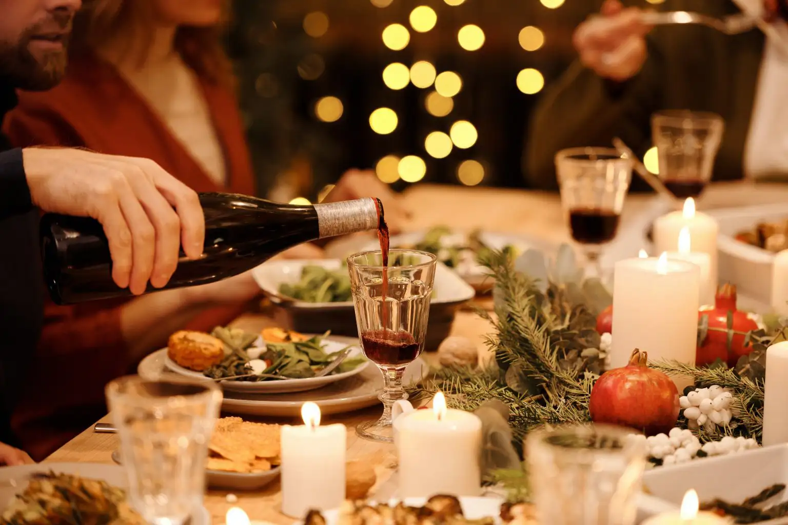 Person pouring red wine into a glass at a candlelit holiday dinner table