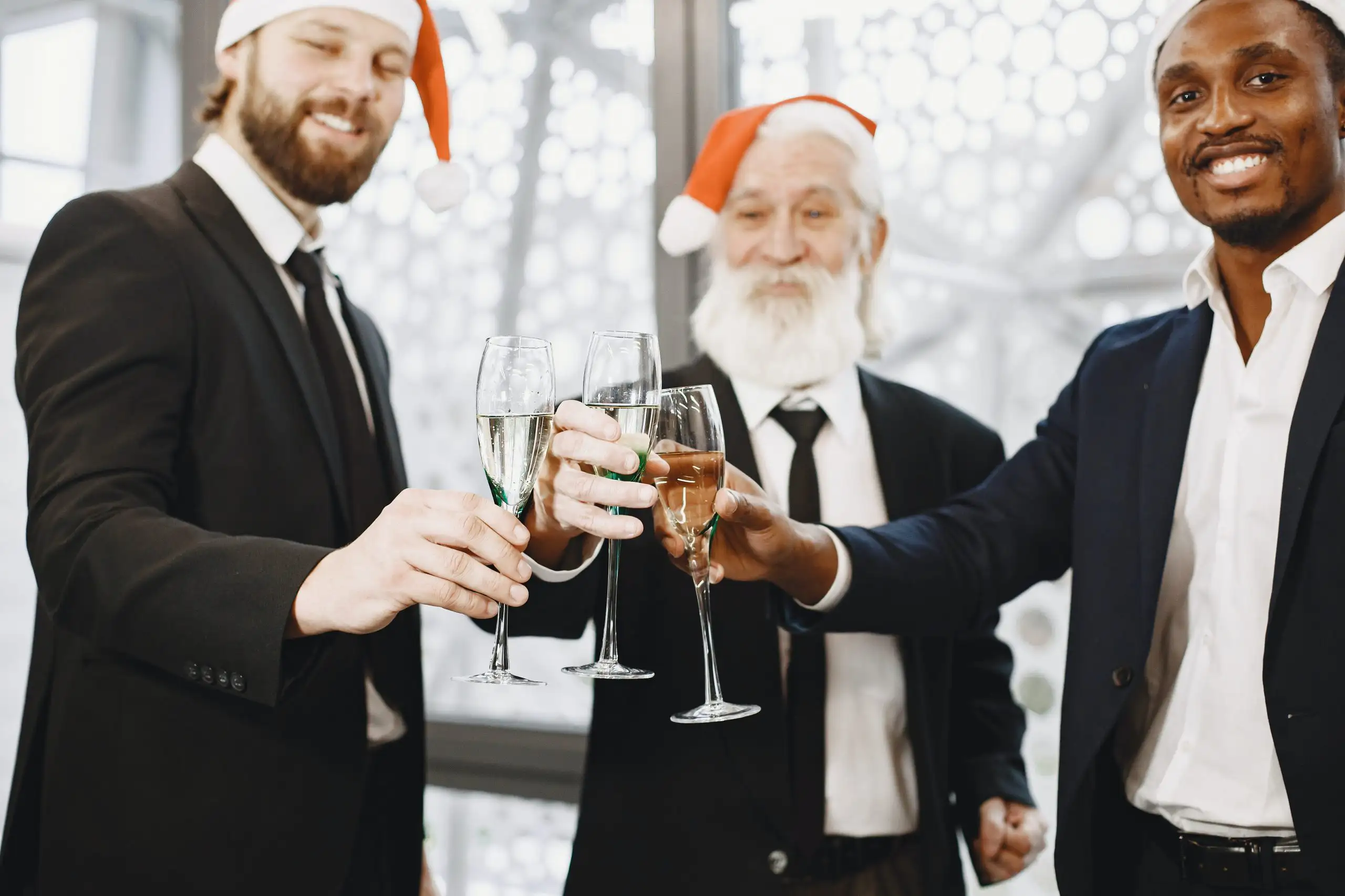 Three men in suits with Santa hats toasting with champagne glasses during a holiday celebration