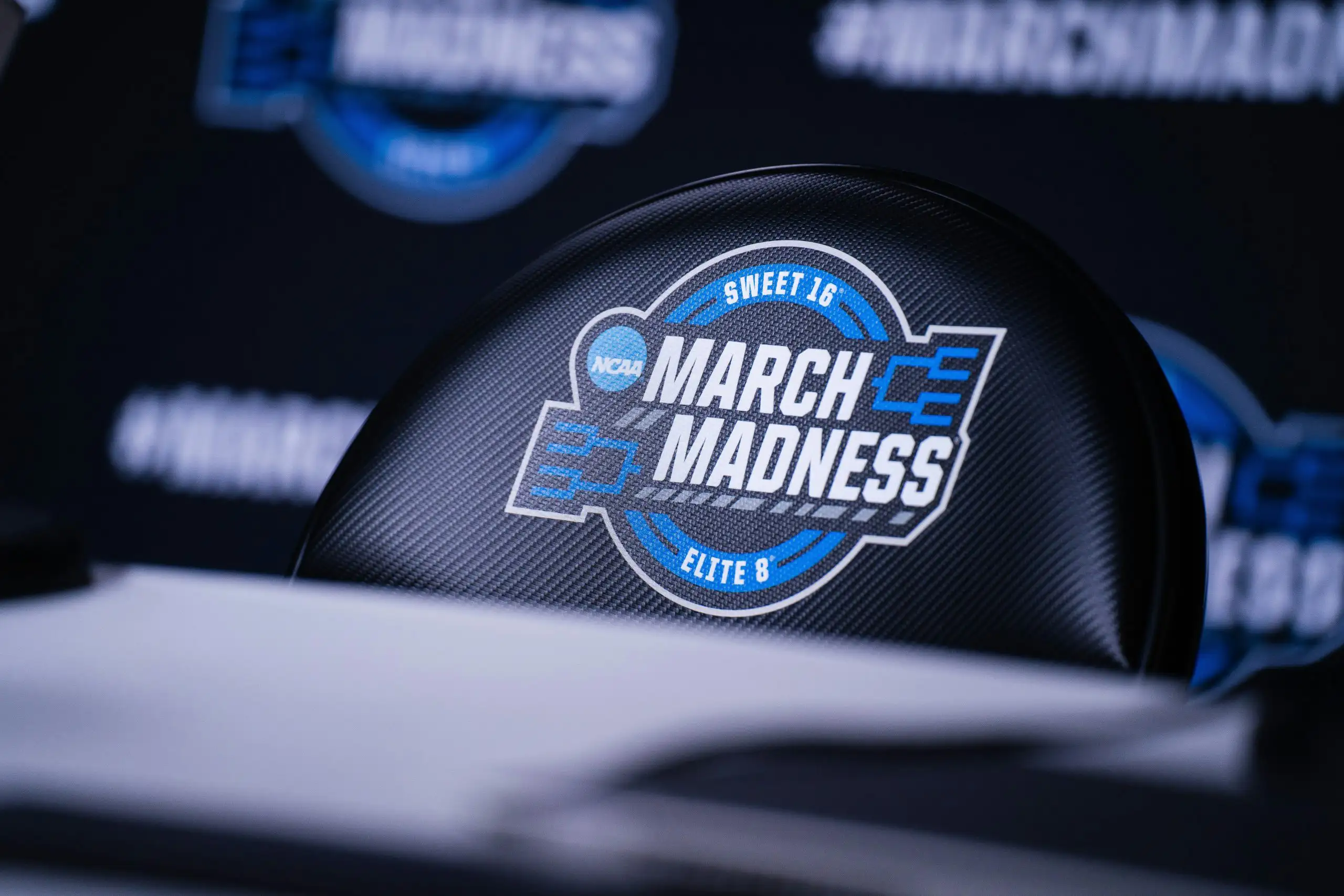 Close-up of the NCAA March Madness Elite 8 logo on a chair during a press conference.