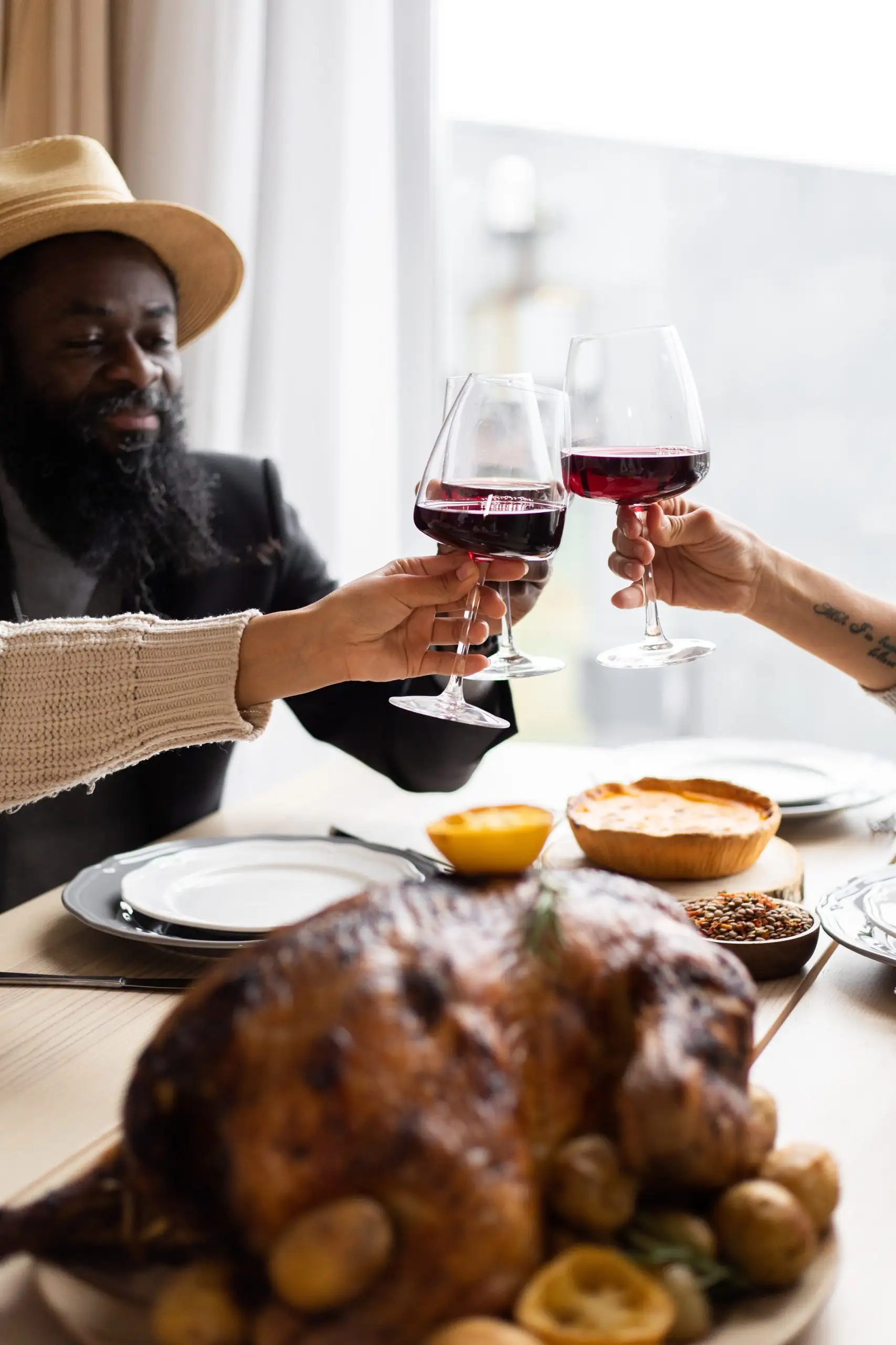 People toasting with glasses of red wine during a festive dinner with roast turkey and side dishes.