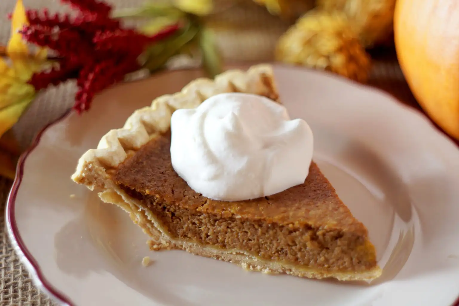 A slice of pumpkin pie topped with a dollop of whipped cream on a decorative plate.