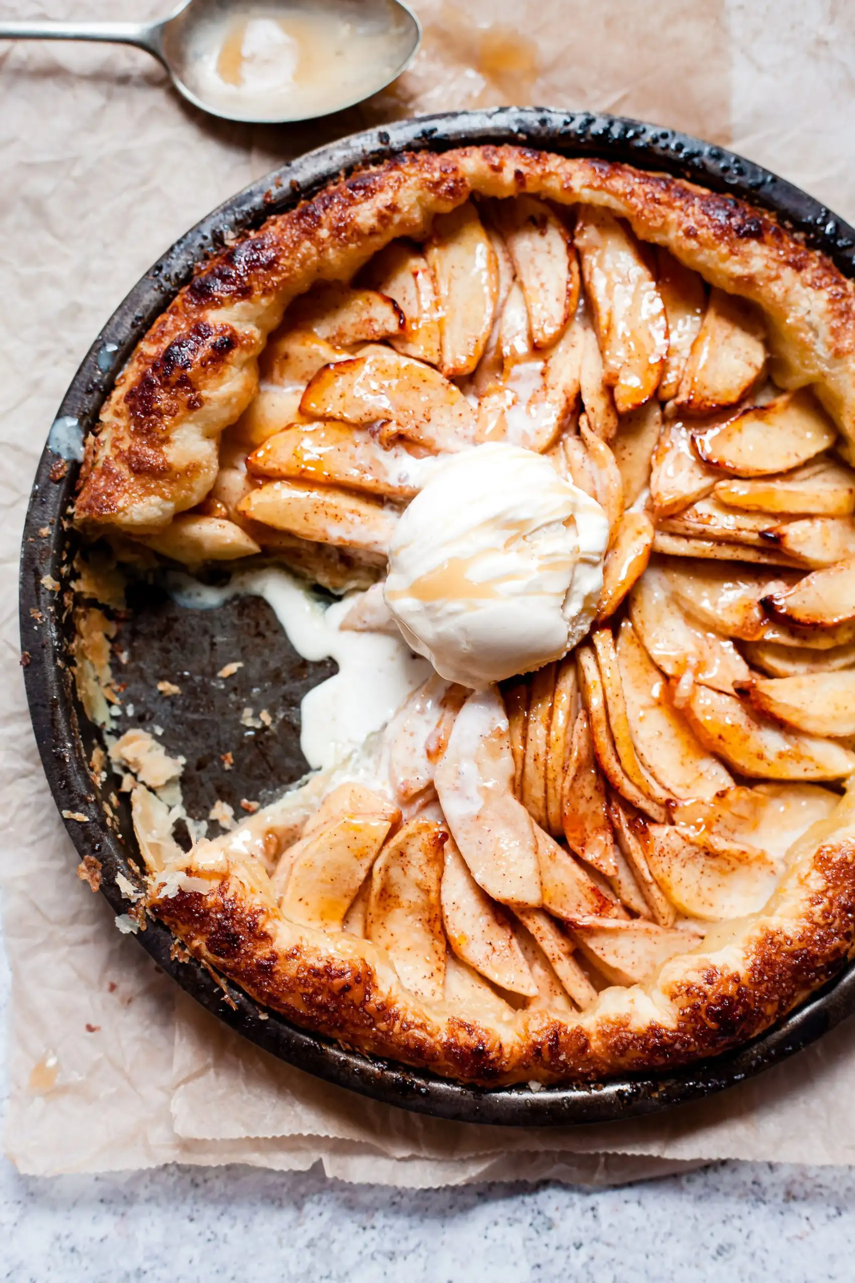 A rustic apple tart with a flaky golden crust topped with a melting scoop of vanilla ice cream and caramel drizzle.