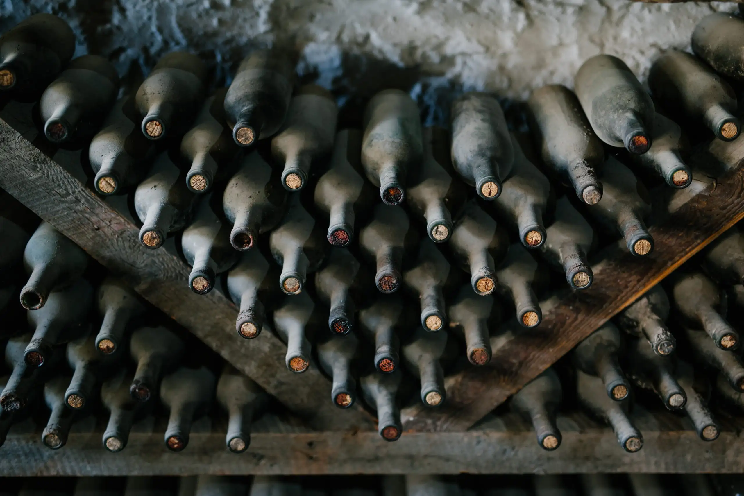 Rows of dusty vintage wine bottles stored horizontally in a rustic wine cellar