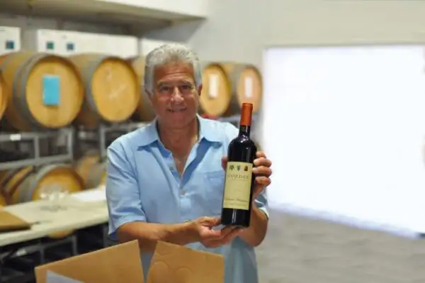 Winemaker holding a bottle of red wine in a cellar with wooden barrels in the background