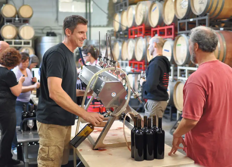 Worker filling wine bottles using a bottling machine inside a winery production area